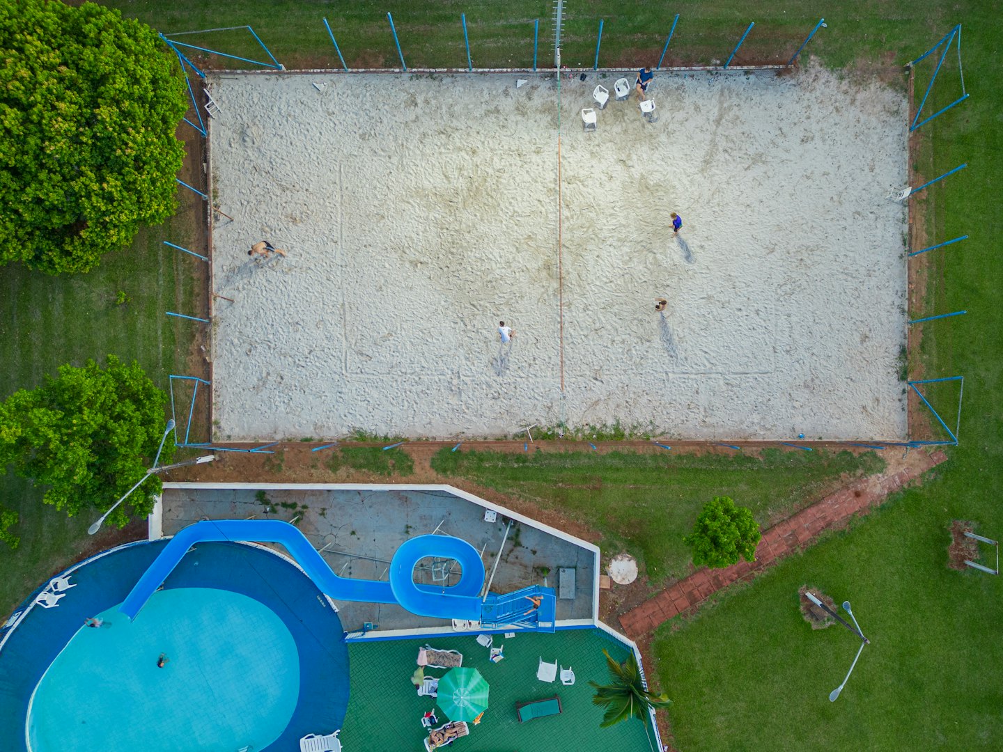 People play volleyball beside a pool with a water slide.