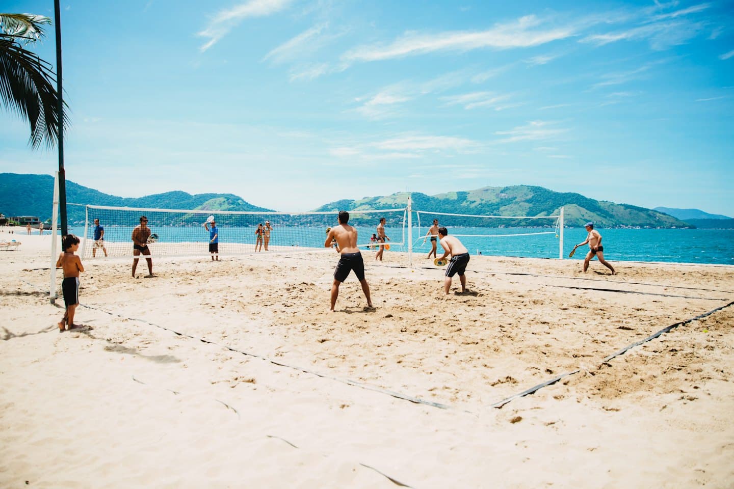 Men and a boy playing beach tennis on a sunny day.