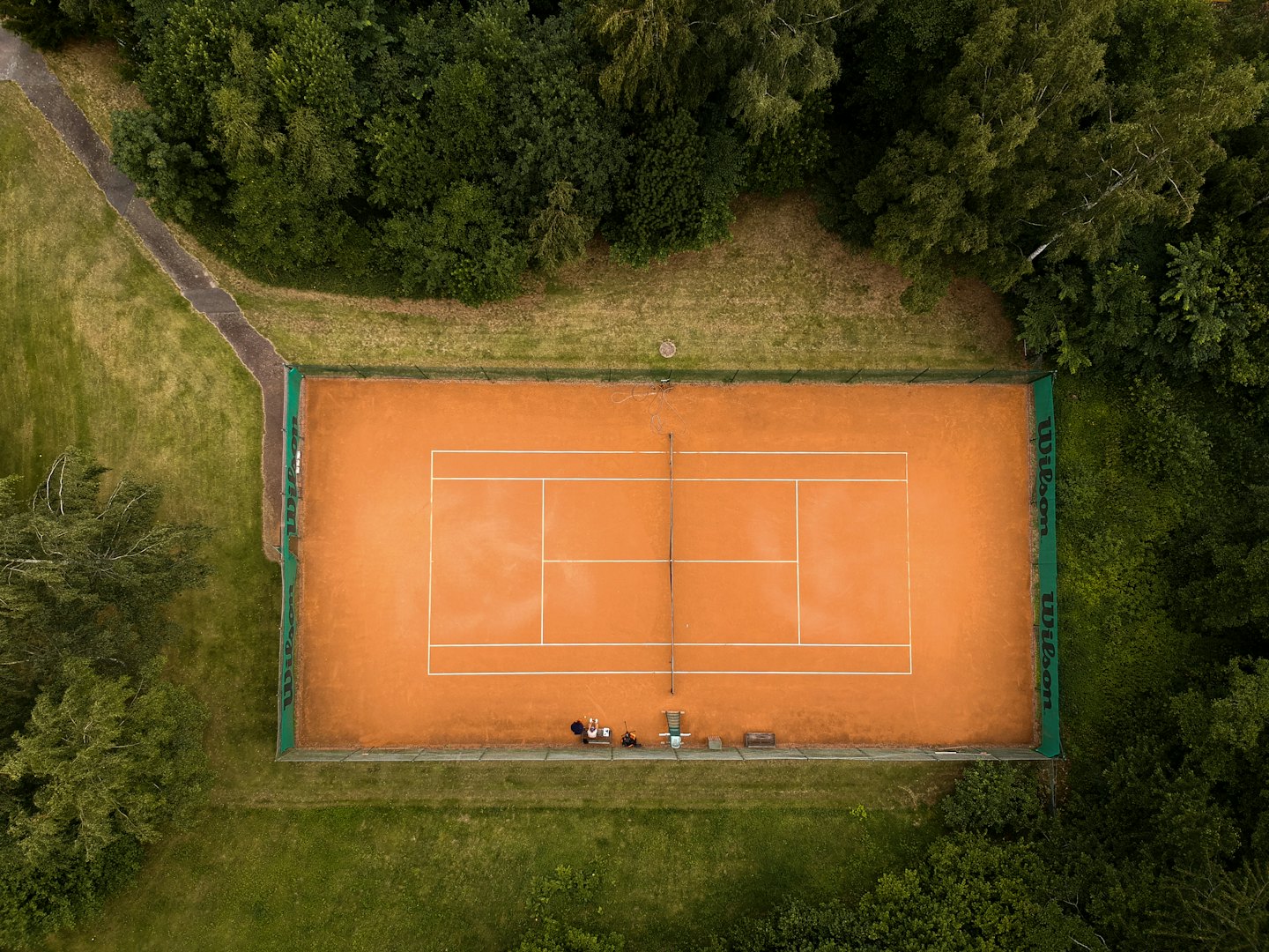 Two people sit on a bench beside a clay tennis court.