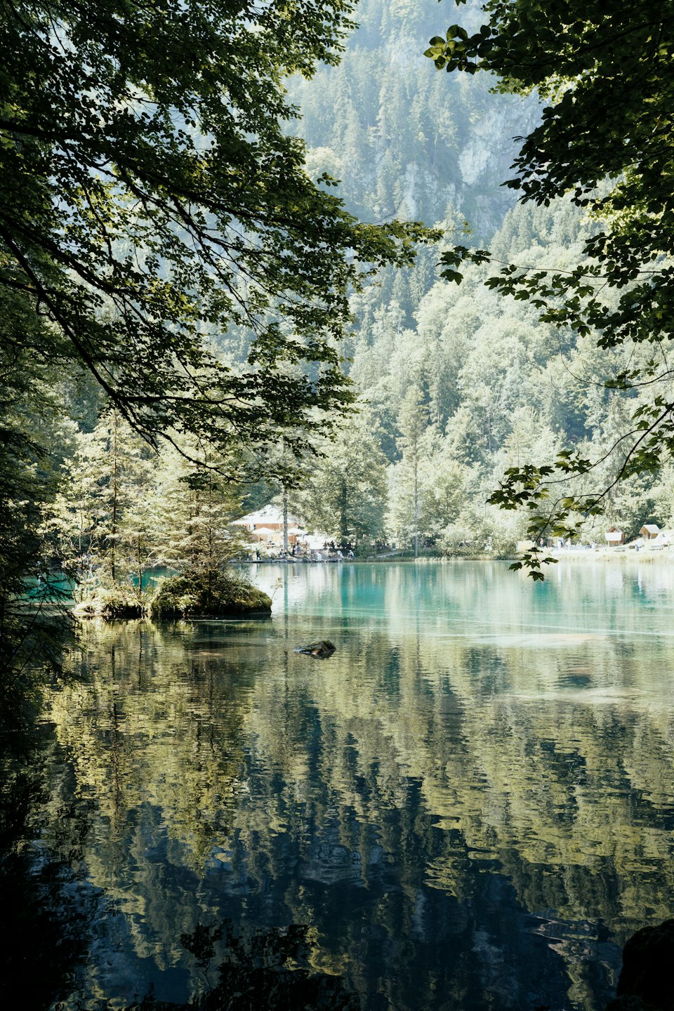 Turquoise lake reflects dense forest and mountains near a village.